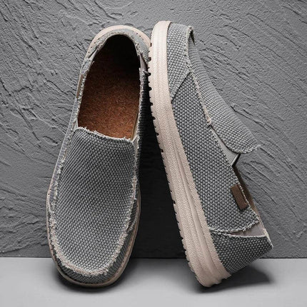 Zapatos informales de lona gris, transpirables, para hombre sobre fondo texturizado.