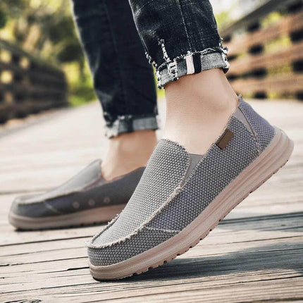 Hombre caminando con zapatos informales de lona gris transpirables, ideales para uso diario. Comodidad y estilo casual.