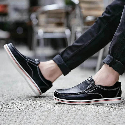 Hombre luciendo zapatos mocasín de cuero negro, estilo casual, con suela blanca y detalles en negro.